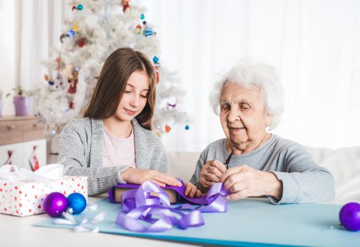 Smiling grandmother with granddaughter decorating gifts with purple paper together at Christmas