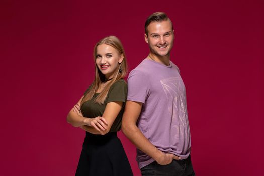 Young nice couple posing in the studio, express emotions and gestures, smiling, on a burgundy background with copy space for your advertisement or written text.