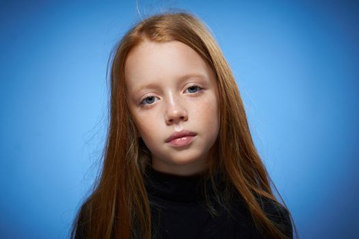 redhead girl with freckles on her face posing close-up blue background. High quality photo