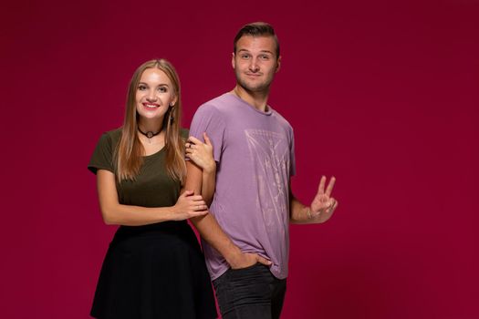 Young nice couple posing in the studio, express emotions and gestures, smiling, on a burgundy background with copy space for your advertisement or written text.