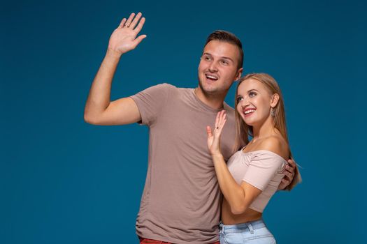 Hello. Portrait of happy couple on blue background. Couple man and woman hugging and looking away