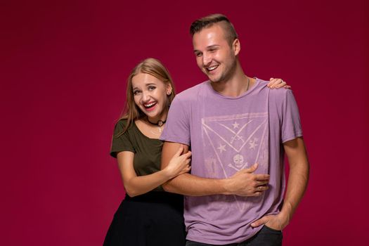 Young nice couple posing in the studio, express emotions and gestures, smiling, on a burgundy background with copy space for your advertisement or written text.