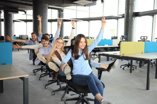 Young cheerful business people dressed in casual clothing are having fun on rowing chairs in a modern office