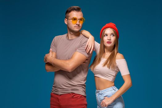 Studio lifestyle portrait of two best friends hipster wearing stylish bright outfits, hats, denim shorts and glasses, going crazy and having great time together. Indoor studio shot, isolated on blue background.