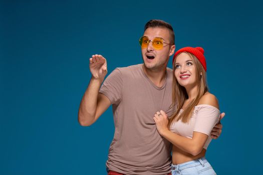 Surprised couple in casual clothes pointing with their index fingers up looking there with great astonishment isolated over blue background with copy space for your advertisement or written text.