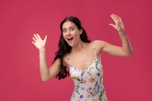 Portrait of beautiful happy young brunette woman and greeting gesture on the pink background