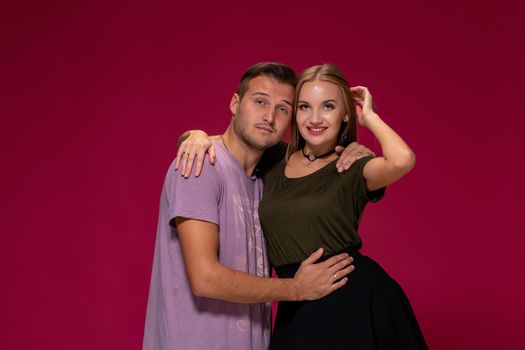 Young nice couple posing in the studio, express emotions and gestures, smiling, on a burgundy background with copy space for your advertisement or written text.