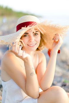 Caucasian cute girl in hat sitting on shingle beach. Concept of summer vacations and beauty.