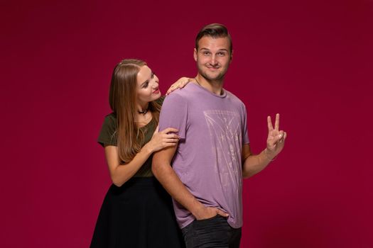 Young nice couple posing in the studio, express emotions and gestures, smiling, on a burgundy background with copy space for your advertisement or written text.