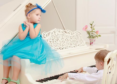 Funny kids posing near the old white Grand piano. The boy presses the button , and the girl helps him.