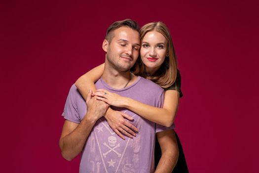 Young nice couple posing in the studio, express emotions and gestures, smiling, on a burgundy background with copy space for your advertisement or written text.