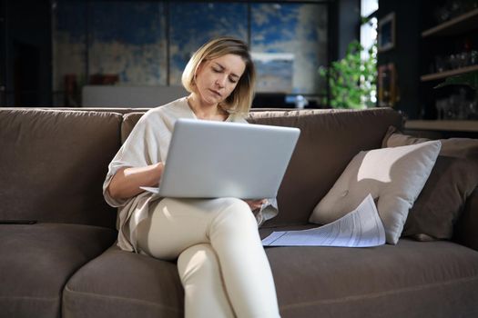 Smiling business woman sit on couch watching webinar on laptop. Happy middle aged woman study on online distant course