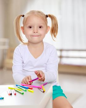 The concept of pre-school education of the child among their peers . in gaming room with a large arched window.Pretty little blonde girl drawing with markers at the table.