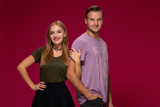 Young nice couple posing in the studio, express emotions and gestures, smiling, on a burgundy background with copy space for your advertisement or written text.