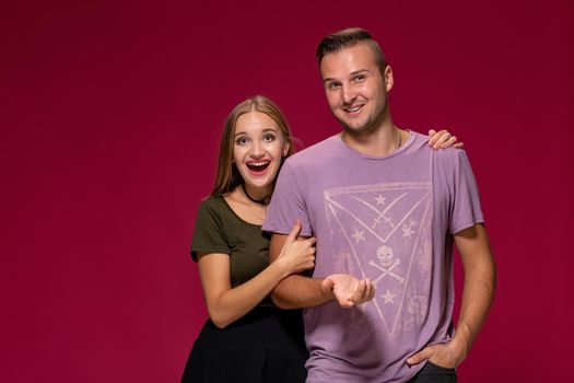 Young nice couple posing in the studio, express emotions and gestures, smiling, on a burgundy background with copy space for your advertisement or written text.