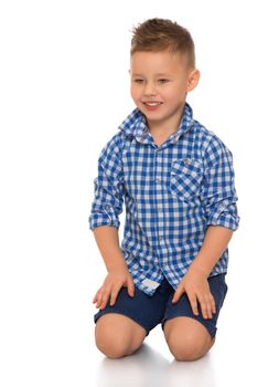 Beautiful little boy in shirt with short sleeves and shorts. The boy sits on the floor. - Isolated on white background