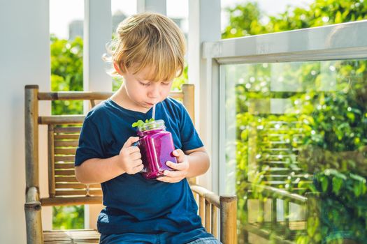 The boy holds smoothies from a dragon fruit with a mint leaf and a drinking straw.