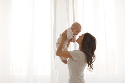 Happy smiling mother with baby having fun together on white of the curtains of the window background