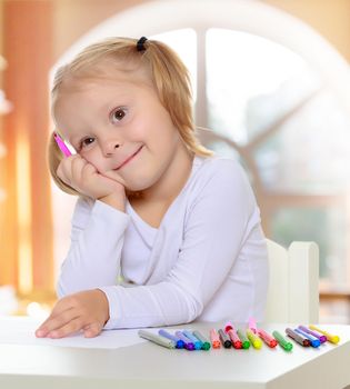 Adorable little blonde girl with white t-shirts without a pattern, draws markers at the table on a white sheet of paper. The girl rested her head on the arm , it's about something thought . close-up.