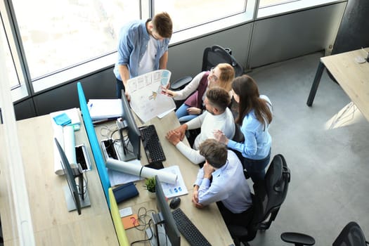 Top view of young modern colleagues in smart casual wear working together while spending time in the office