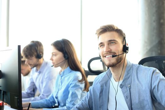 Portrait of call center worker accompanied by his team. Smiling customer support operator at work