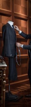 Unrecognizable tailor man measuring suit on dummy with tape-measure.
