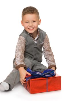 Beautiful little boy in gray a new costume, holding a box with a gift . the boy sits on the floor - Isolated on white background