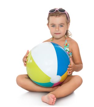 Beautiful little girl in sunglasses and bathing suit. Girl holding in hands in front of a large striped ball. Girl sitting on the floor