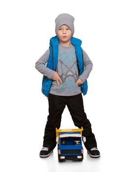 Beautiful little boy in the autumn is to walk on the street in warm pants , a jacket and a cap. A boy plays with a machine - Isolated on white background