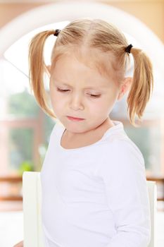 Beautiful little blonde girl with pigtails on his head, white t-shirts without a pattern. The girl is upset about something. Close-up.