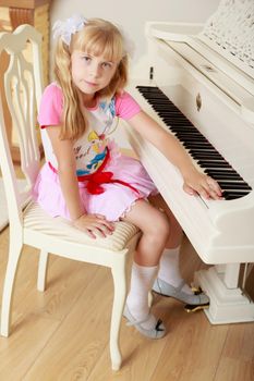 Cute little blonde girl sitting next to the piano facing away from the tool