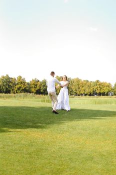 Happy groom and bride dancing on grass. Concept of wedding photo session on open air and nature.