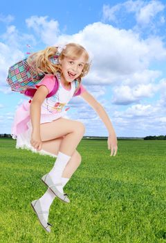 Cheerful little girl in a pink short skirt hurries to school.On the background of grass and blue sky with clouds.