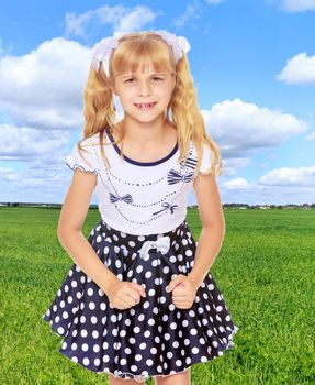 Beautiful little blonde girl in polka dot dress,the girl upset. Close-up.On the background of grass and blue sky with clouds.