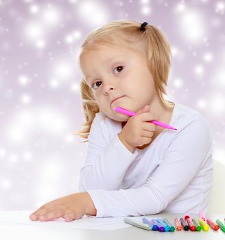 Pretty little blonde girl drawing with markers at the table.The girl thoughtfully looks into the camera.The concept of celebrating the New year, Holy Christmas, or child's birthday on a purple background and white snowflakes.