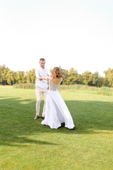 Happy young groom and bride dancing on grass. Concept of wedding photo session on open air and nature.