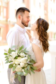 Happy groom kissing bride keeping bouquet of flowers. Concept of love and wedding photo session.