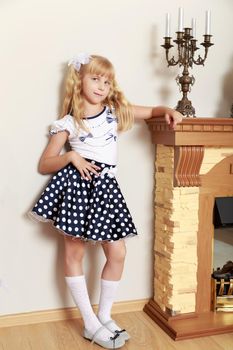 Beautiful little girl in a smart polka-dot skirt costs about the fireplace