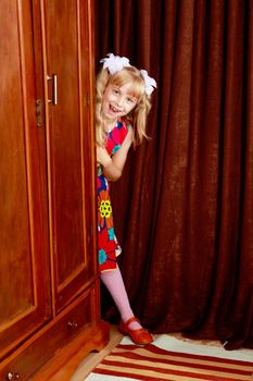 Cute little girl hidden behind an old wardrobe . retro style