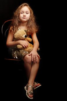 A nice little girl with a teddy bear. Studio photo on a black background. The concept of a happy childhood, publication on the cover of the magazine.
