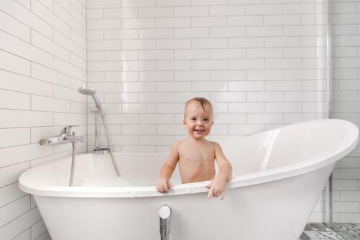 Adorable little wet boy standing and smiling in white bath.