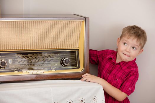Cute little blond boy in red shirt is posing near the old radio.Retro style, surrounded by old things fifties of the last century.