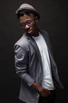 Portrait of a fashionable african american man smiling on black background. A nice guy in a gray jacket and a white T-shirt on a dark studio background. Belt portrait