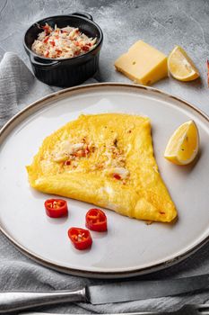 Fried breakfast omelette with a crab meat and cheese, on plate, on gray background
