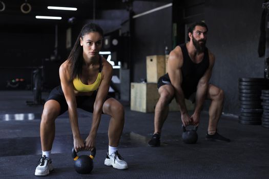 Fit and muscular couple focused on lifting a dumbbell during an exercise class in a gym