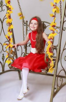 Happy little girl with long brown hair to her waist . Girl in bright red dress. Girl swinging on a swing with his legs