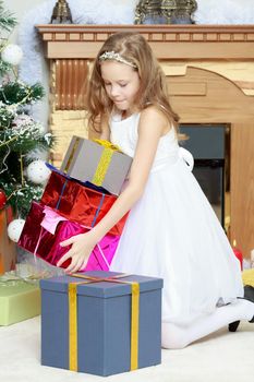 Cute little Princess white dressy holiday dress near the Christmas tree. Girl holding in hands a big box with a gift.