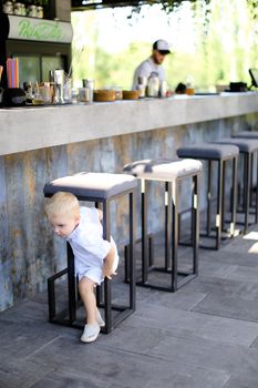 Little cute male baby wearing white clothes and playing outside at street cafe. Concept of childhood.