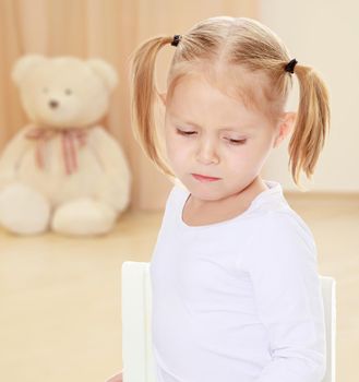 The concept of preschool development of the child ,against a child's room where in the background a Teddy bear.Distressed small, blonde girl with white t-shirts without a pattern.