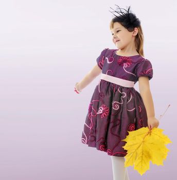 On a purple background, smooth transition from dark to light. Caucasian little girl dressed in brown dress. She is holding a bouquet of maple leaves. Turning sideways to the camera.